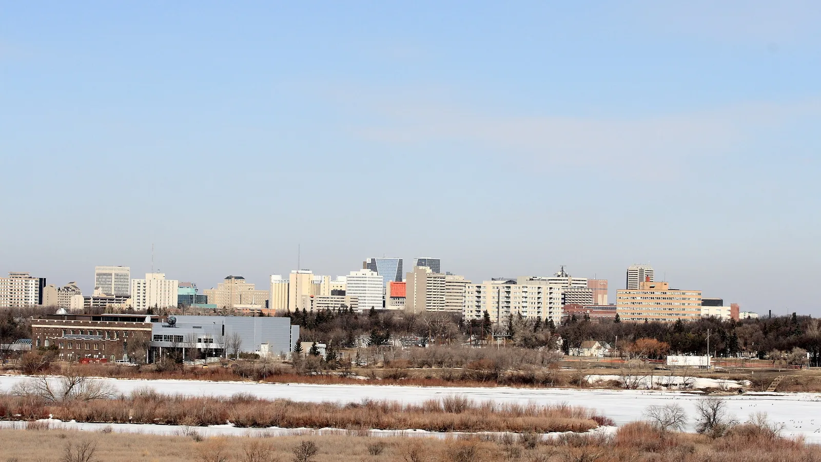 Regina's downtown skyline seen at a distance across open ground, with low buildings and a few taller towers under a clear sky.