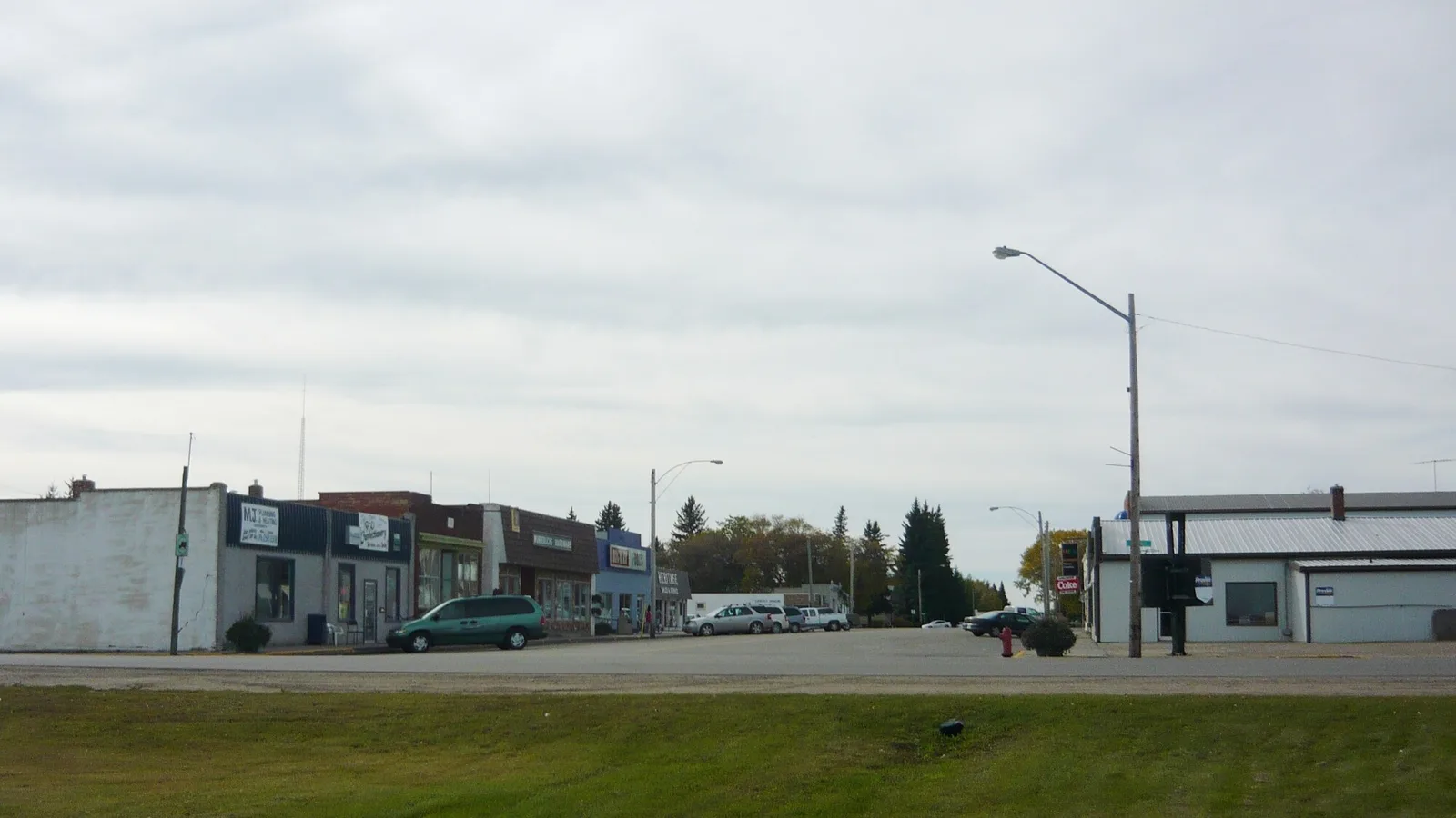 A small-town Saskatchewan main street with modest low-rise storefronts under a wide prairie sky