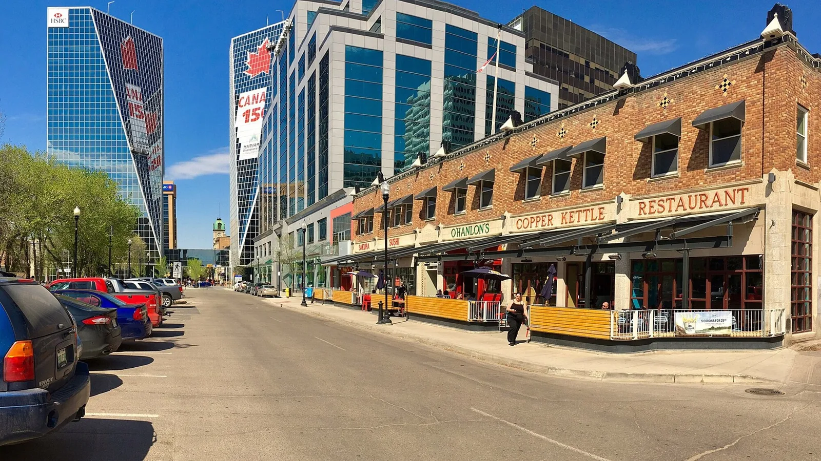 A Regina street seen from the roadway, with brick storefronts, a red Regina sign and office towers standing behind.