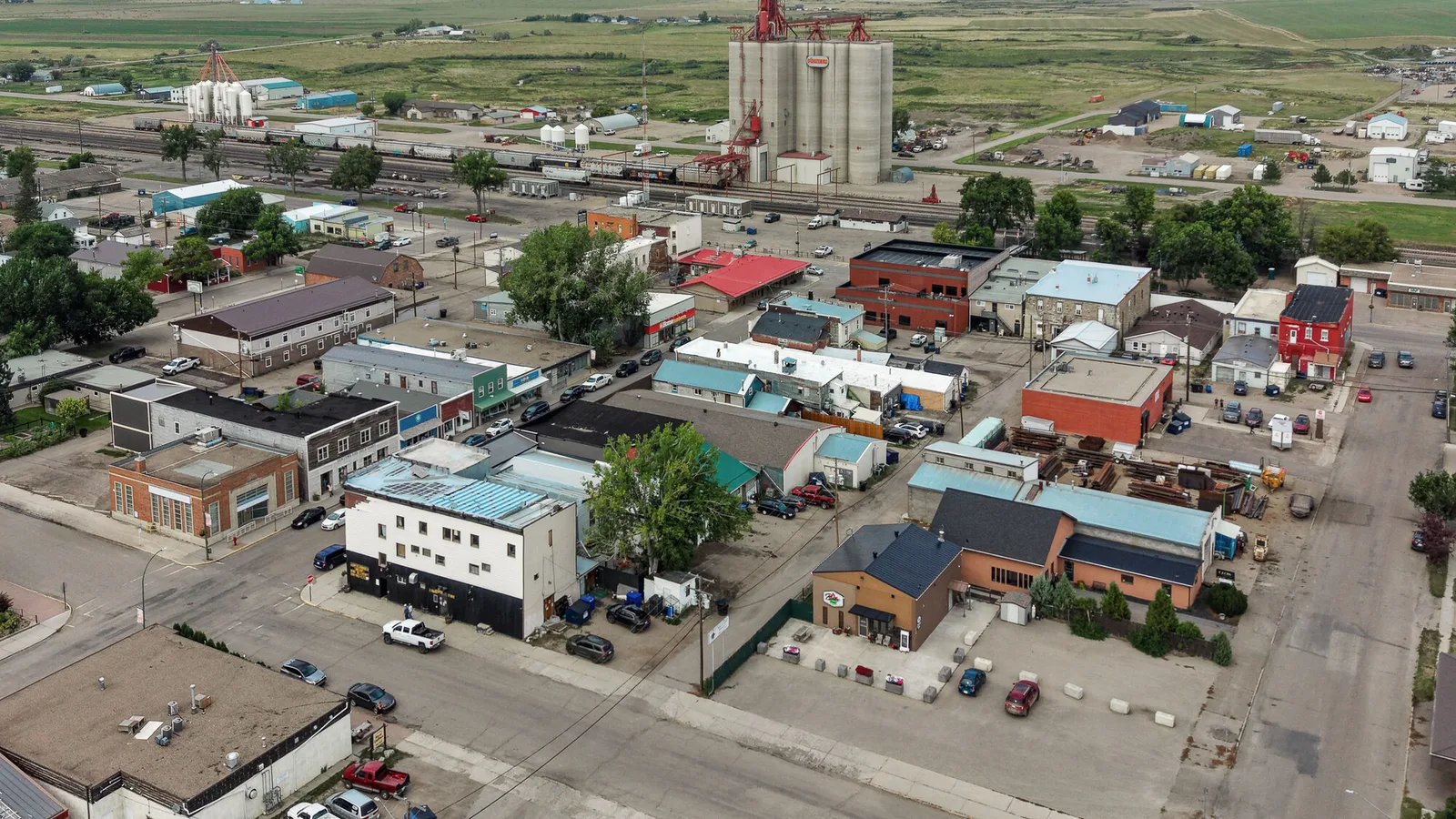 An aerial view of Maple Creek, Saskatchewan, showing a grain elevator, low commercial buildings and streets laid out around the railway.