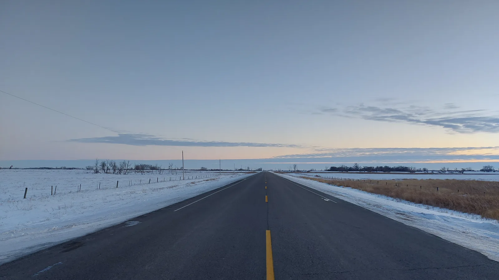A two-lane rural Saskatchewan highway under snow, seen empty toward the horizon.