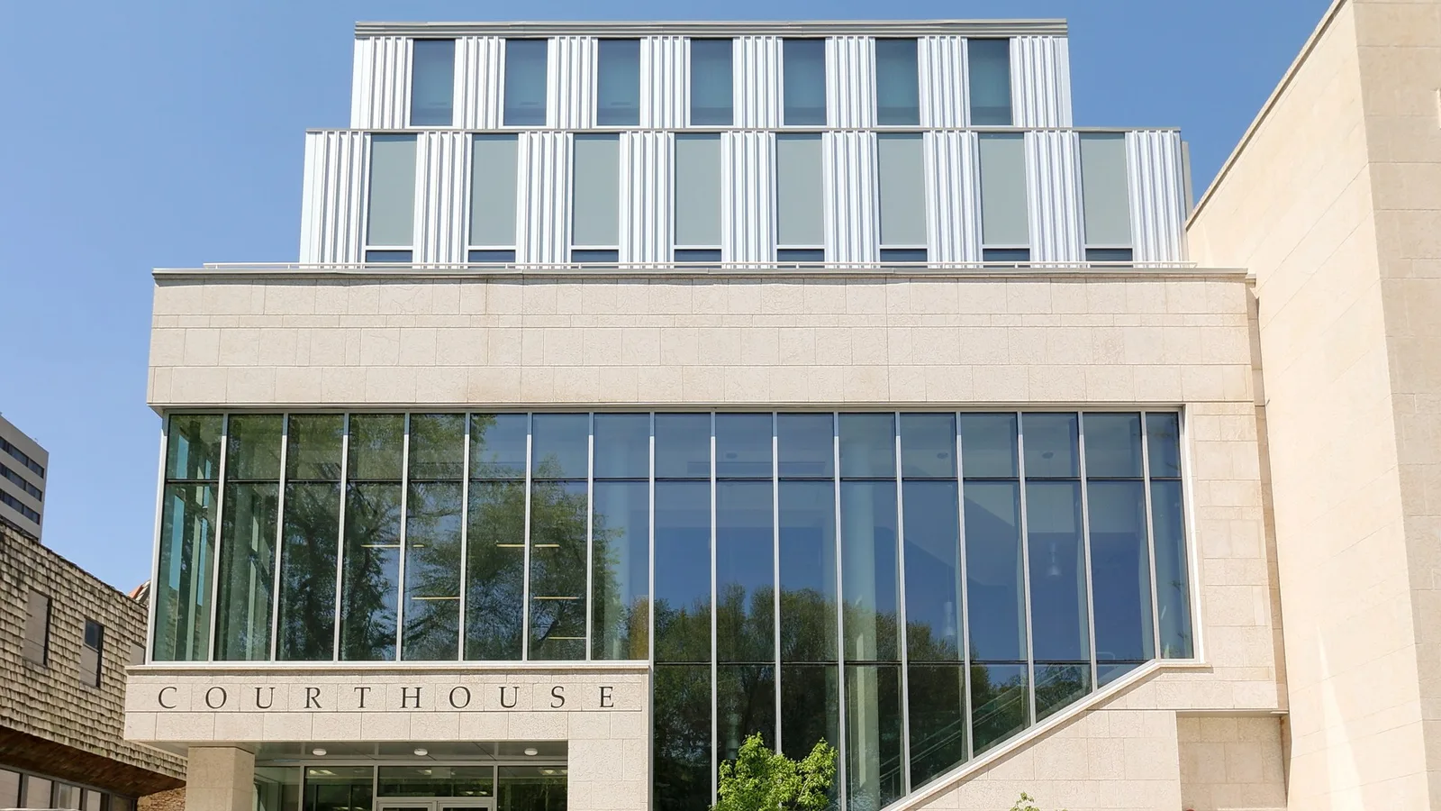 A stone courthouse in Saskatoon with "Courthouse" carved above its glass entrance, seen under a clear blue sky.